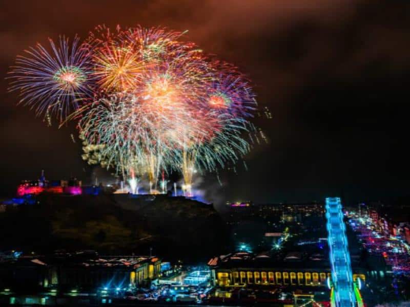 Fireworks display over Edinburgh at night with illuminated structures for New Year's celebration.